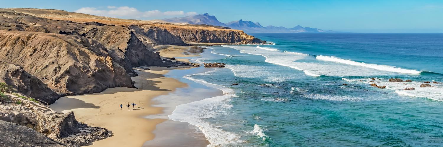 A beach in Spain with blue sea to the right and rocky cliffs to the left A beach in Spain with blue sea to the right and rocky cliffs to the left