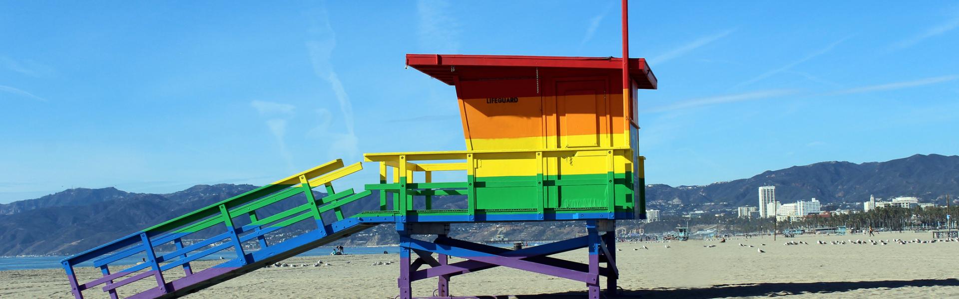 View of a wooden hut painted in rainbow colors standing on a beach. View of a wooden hut painted in rainbow colors standing on a beach.