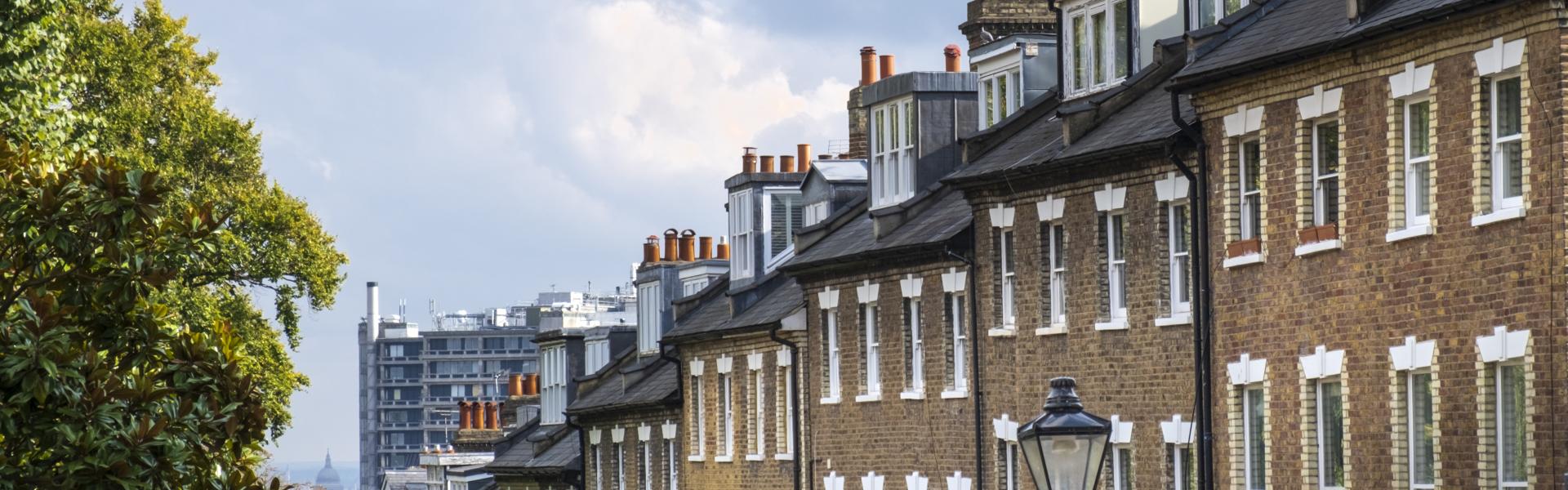 United Kingdom, London, Hampstead village. A view down a steep street of 18th Century Georgian terraced houses with sash windows in Hampstead, a suburb in North London. The Royal Free Hospital, the dome of St. Paul's cathedral and downtown London are visible in the distance