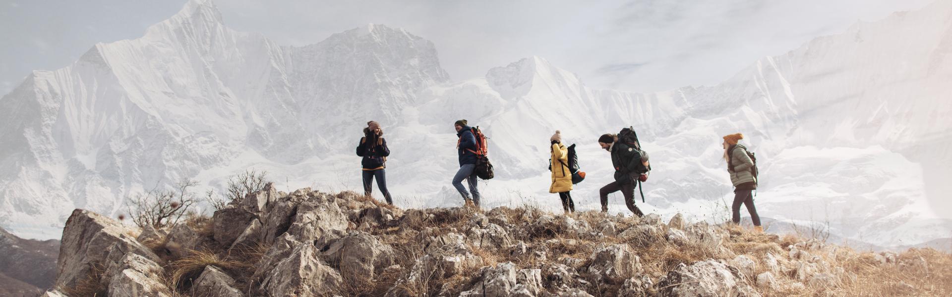 Group of friends hiking and enjoying in a beautiful nature around them. Beautiful snowy mountain peak behind them.