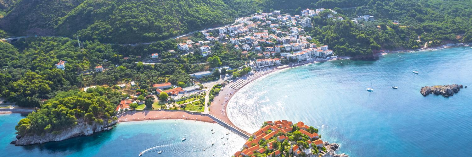 Aerial view of Sveti Stefan ("Saint Stephen"), a fortified island village on the Adriatic coast of Montenegro, connected to the mainland by a narrow causeway. On the island are 15th-century stone villas overlooking an impeccable pink-sand beach and tempting turquoise waters.