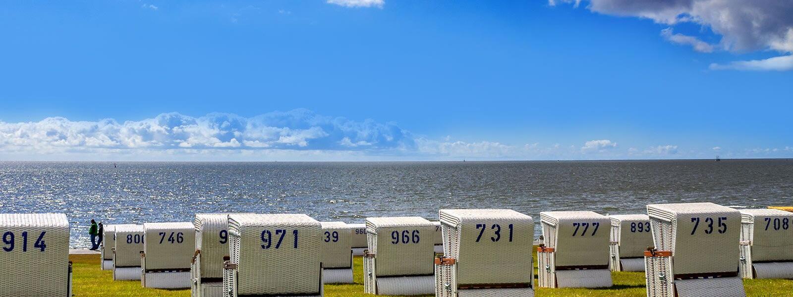 Dithmarschen: Weiße Strandkörbe auf Wiese am Meer
